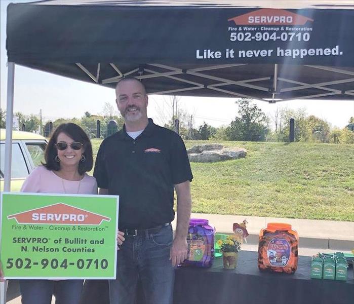 SERVPRO black tent, 2 marketing representatives holding SERVPRO sign, SERVPRO candy boxes on top of table under tent