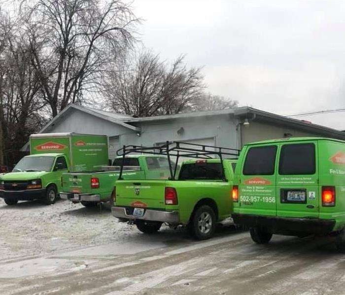 4 SERVPRO trucks located in front of grey commercial building, light snow covering parking lot