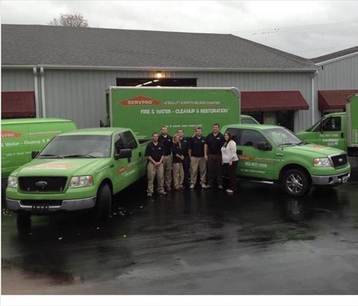 Grey commercial building, red awnings, 5 SERVPRO vehicles, 7 SERVPRO employees